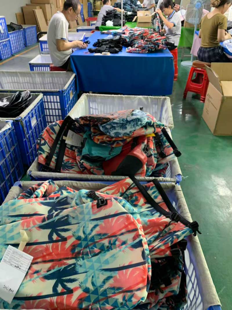 Finished printed roll-top dry backpacks stacked in a cloth-lined bin